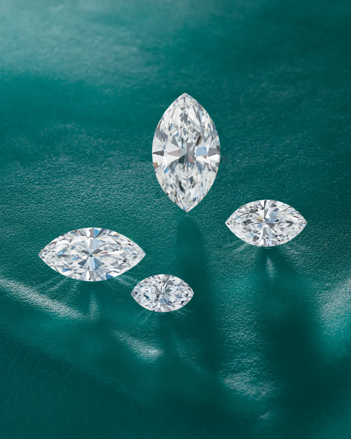 Four marquise-cut diamonds on a teal surface, showcasing their brilliance.