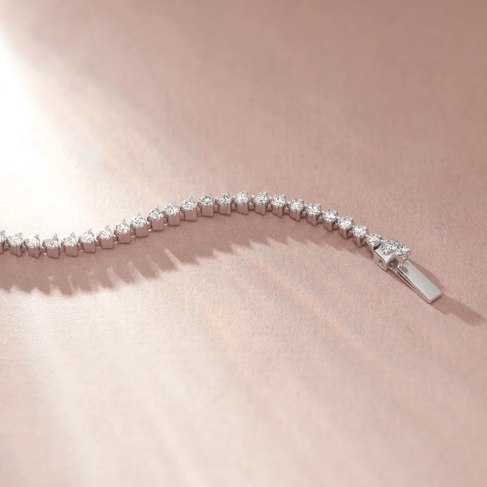 Elegant diamond tennis bracelet on a soft pink background.