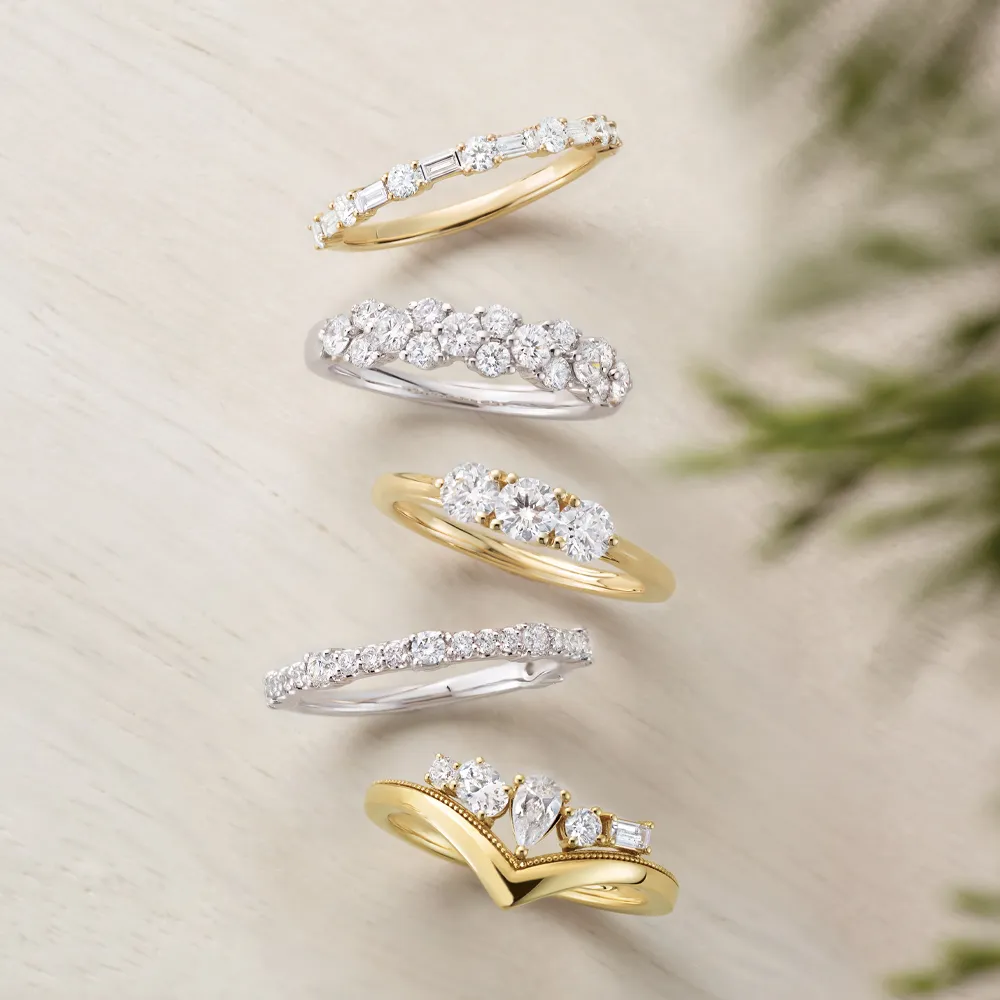 Five gold and silver diamond rings displayed on a light surface.