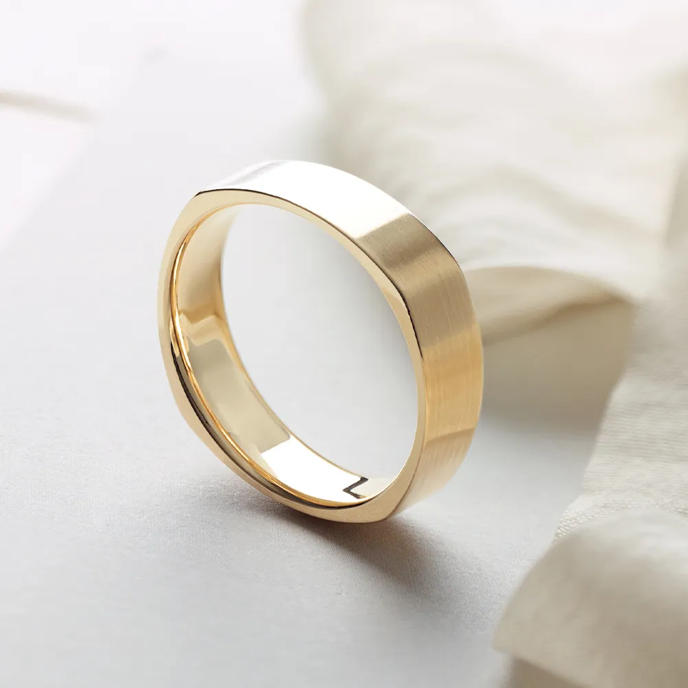 Gold men's wedding band with a brushed finish on a white surface.