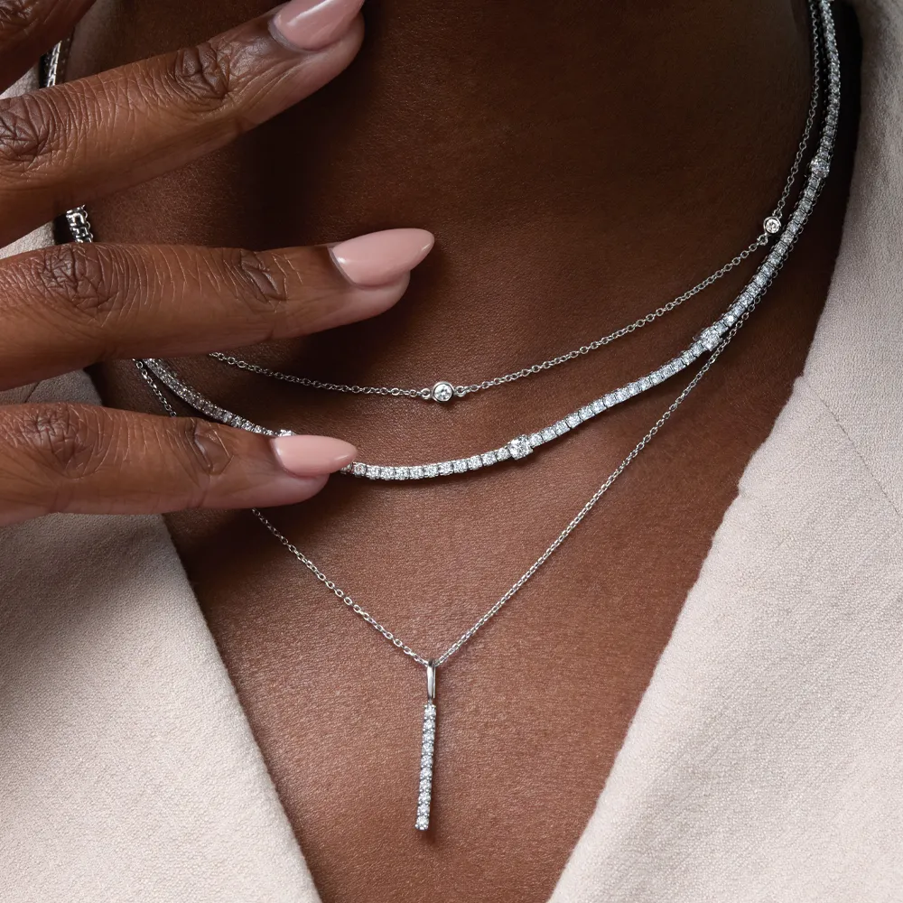 Layered silver necklaces with diamond accents on a person wearing a light top.