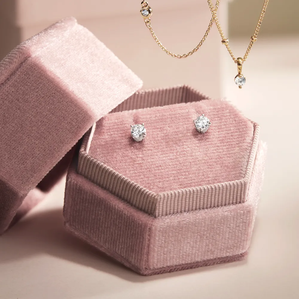 Diamond studs in a pink velvet box with a gold necklace above.