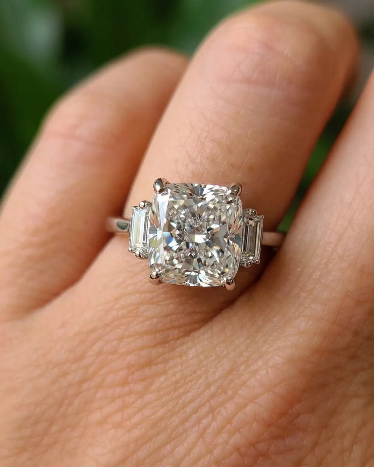 A hand wearing a large, radiant-cut diamond ring with baguette side stones.
