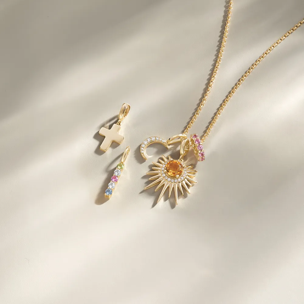 Gold charms including a cross, colorful stones, and sunburst pendant on a chain.