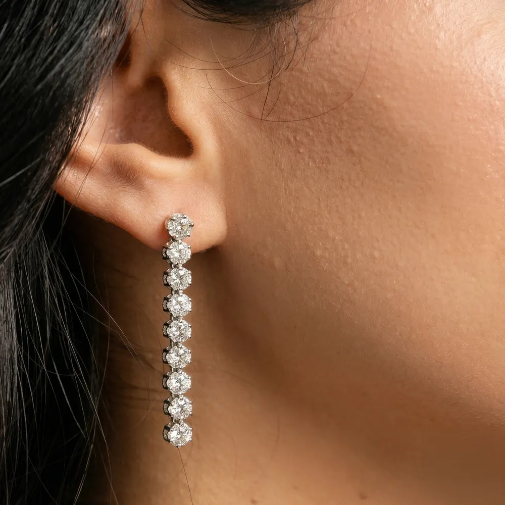 Close-up of a woman's ear wearing a long, sparkling diamond earring.