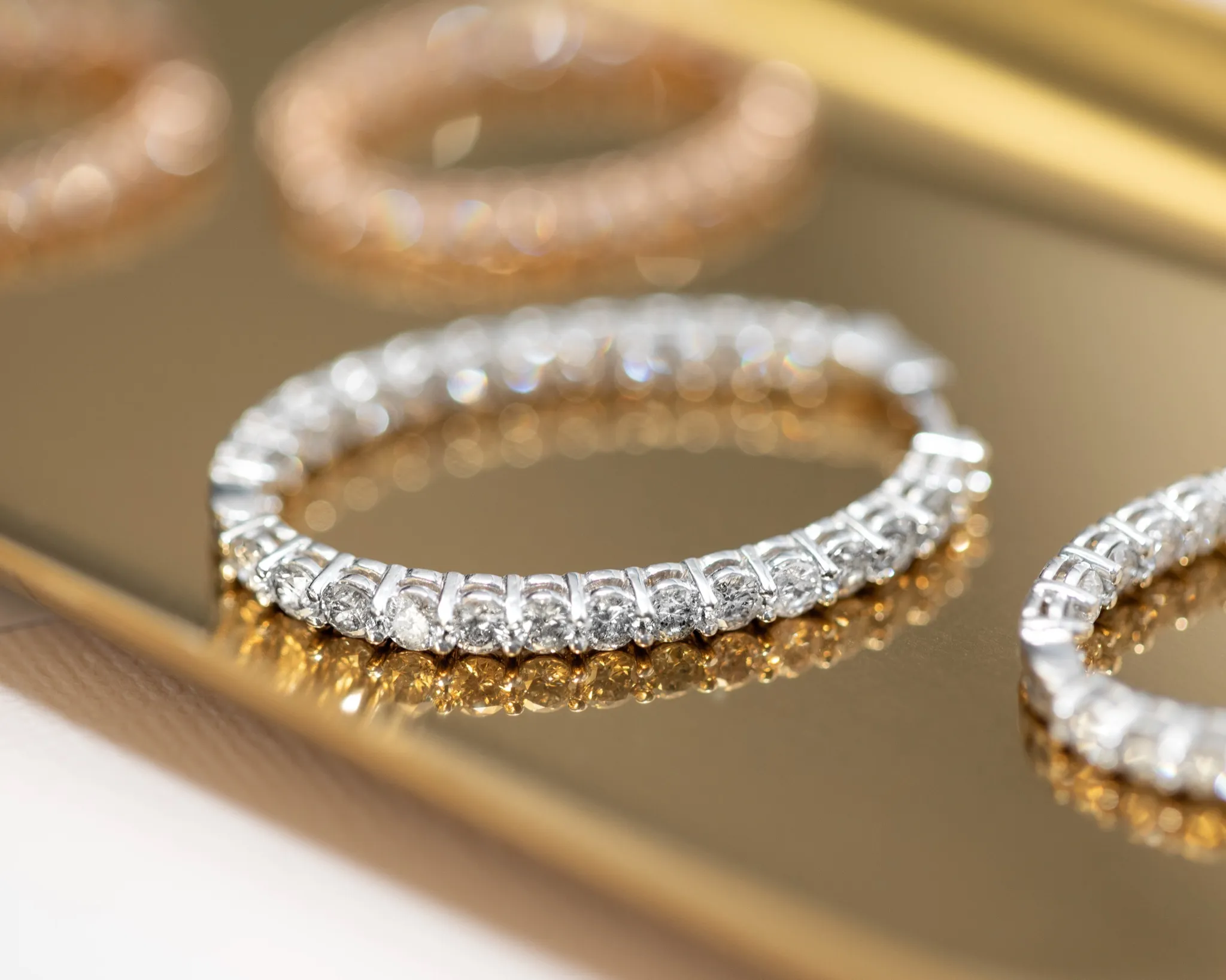 Two diamond engagement rings with halo settings on a reflective surface.