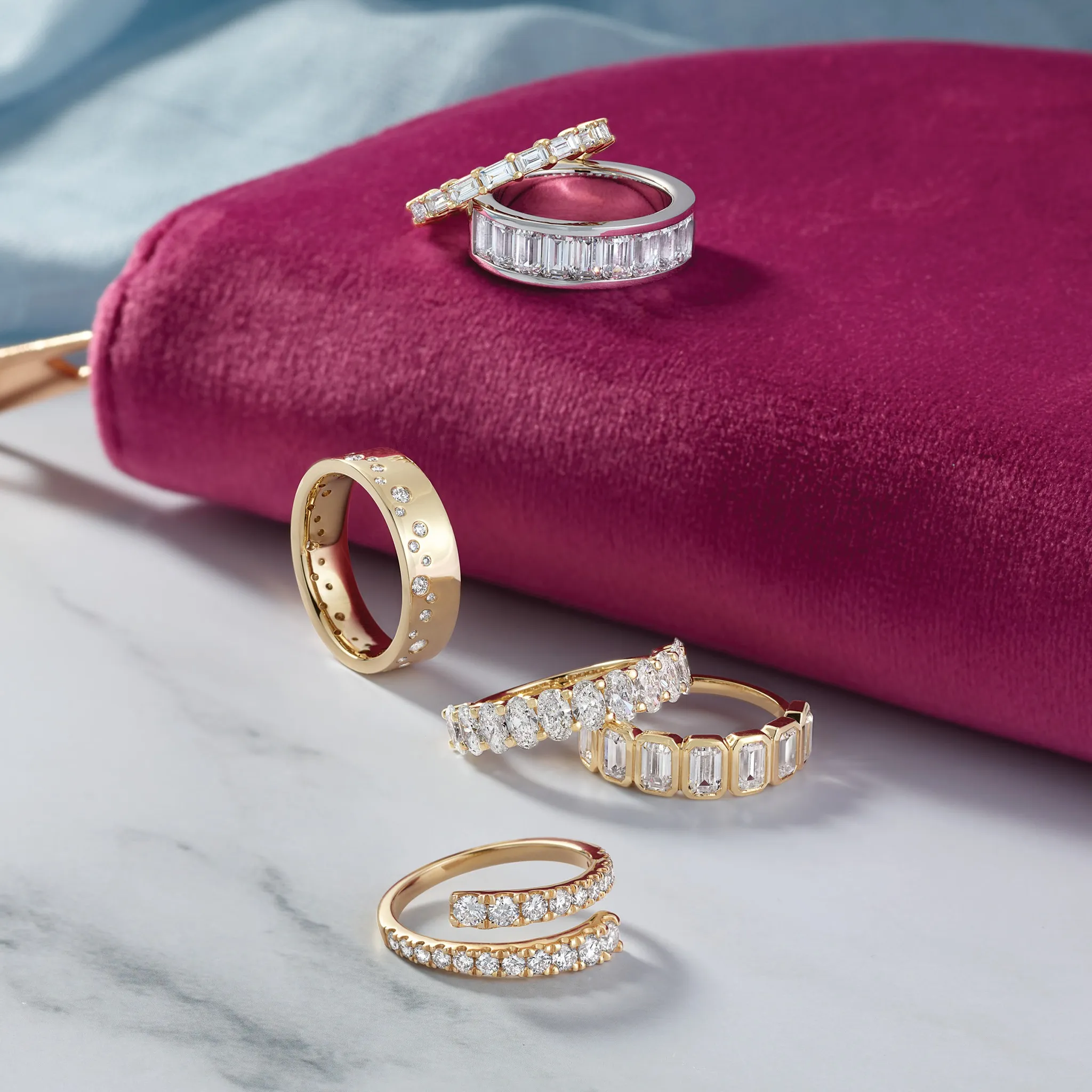 Stacked gold and silver rings with diamonds on a beige background.