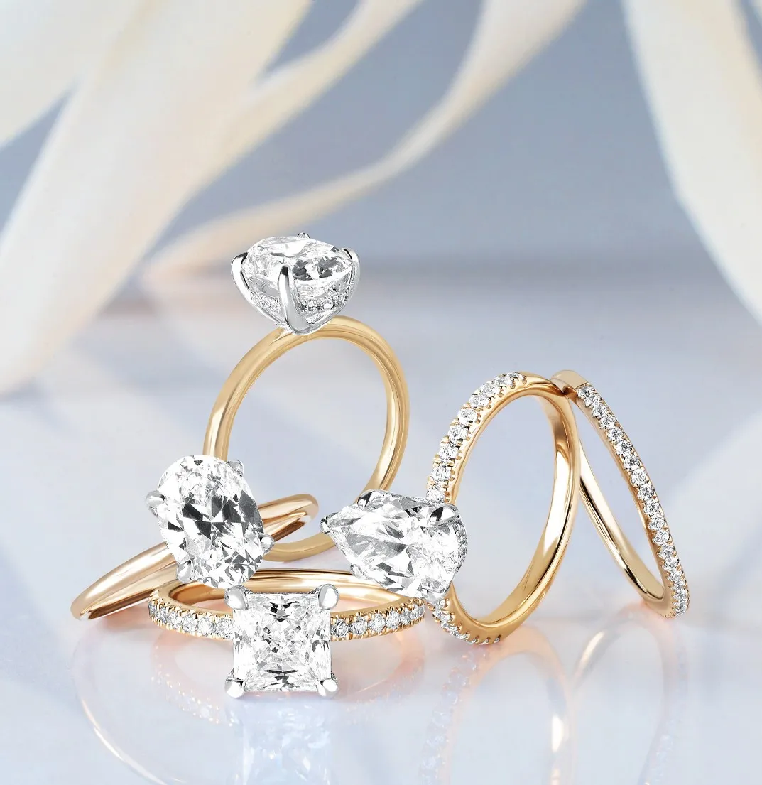 Three rings: a diamond-studded silver ring, a gold ring with a large diamond, and a plain gold band on a soft background.