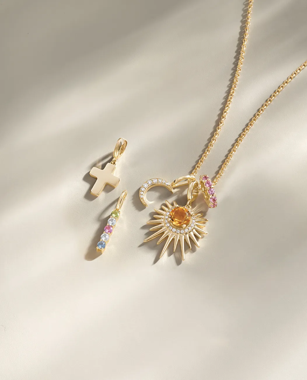 Gold necklace with sun, cross, and colorful charms.