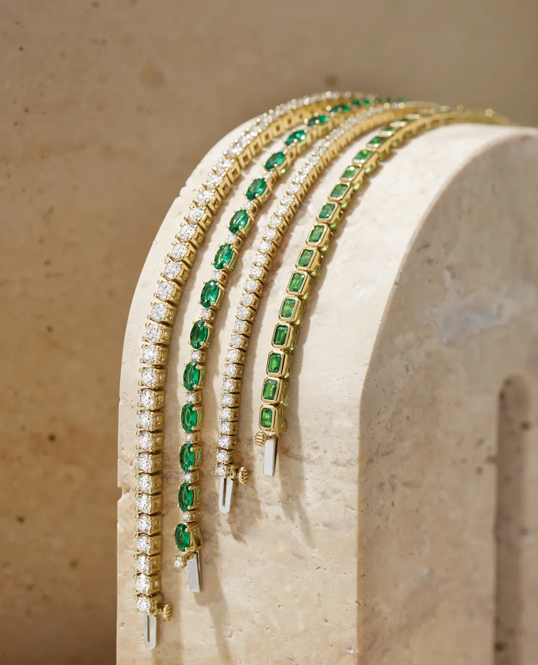 Elegant gold bracelets with emerald and diamond accents displayed on a stone arch.