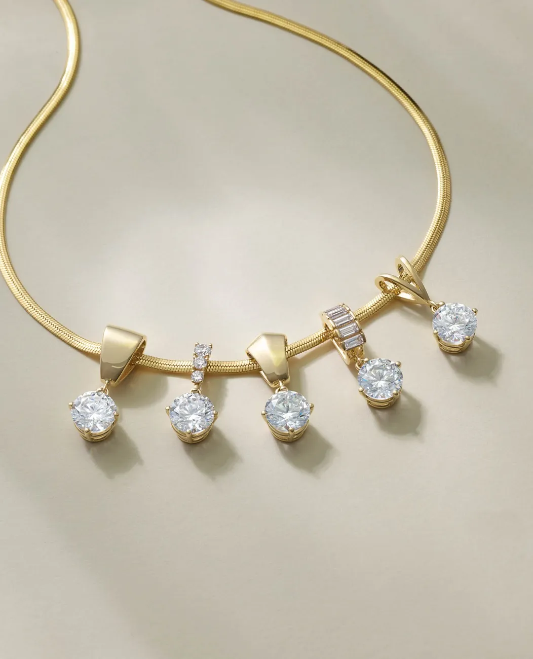 Gold necklace with five diamond pendants on a light background.