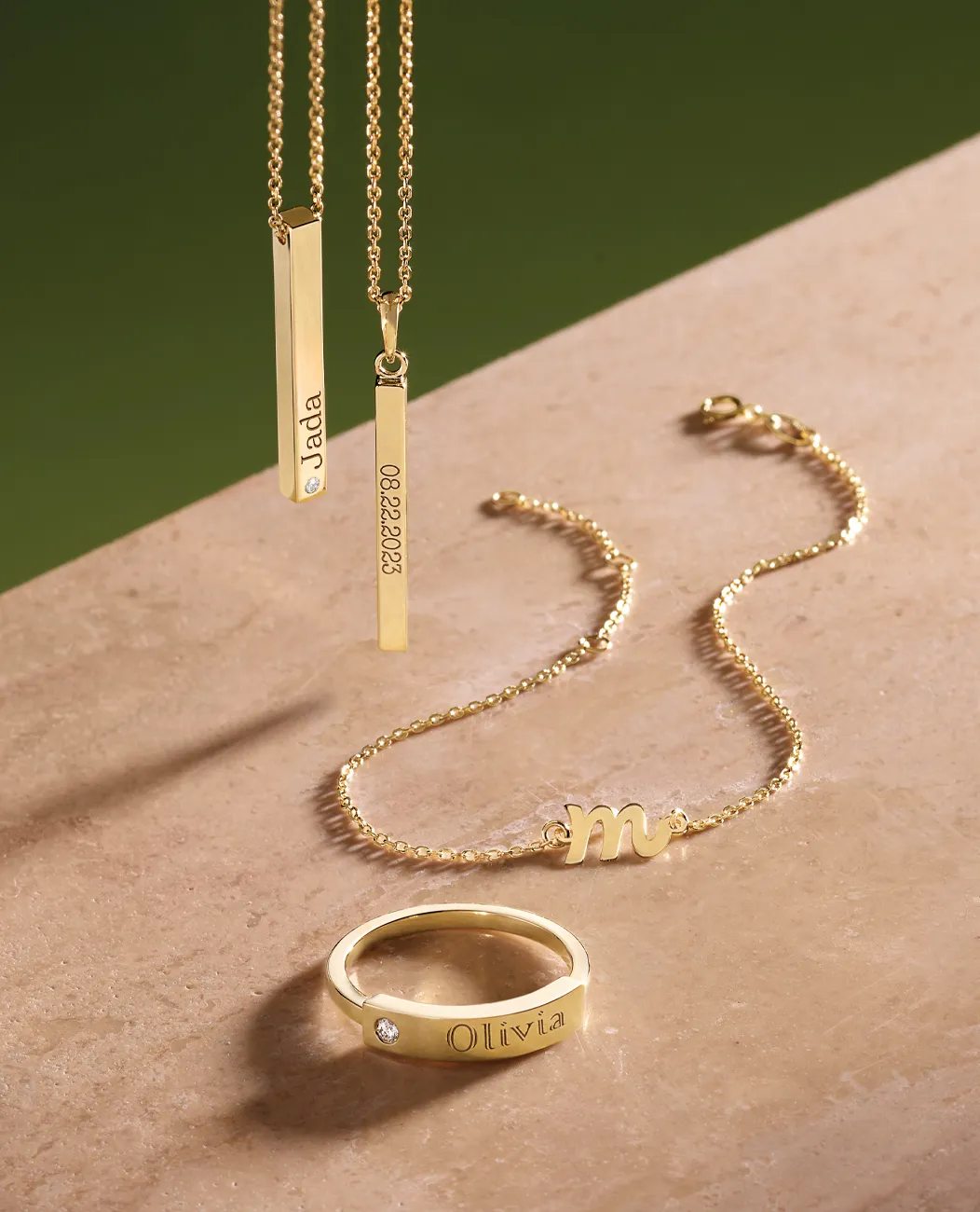 Gold necklaces and ring with personalized engravings on a marble surface.