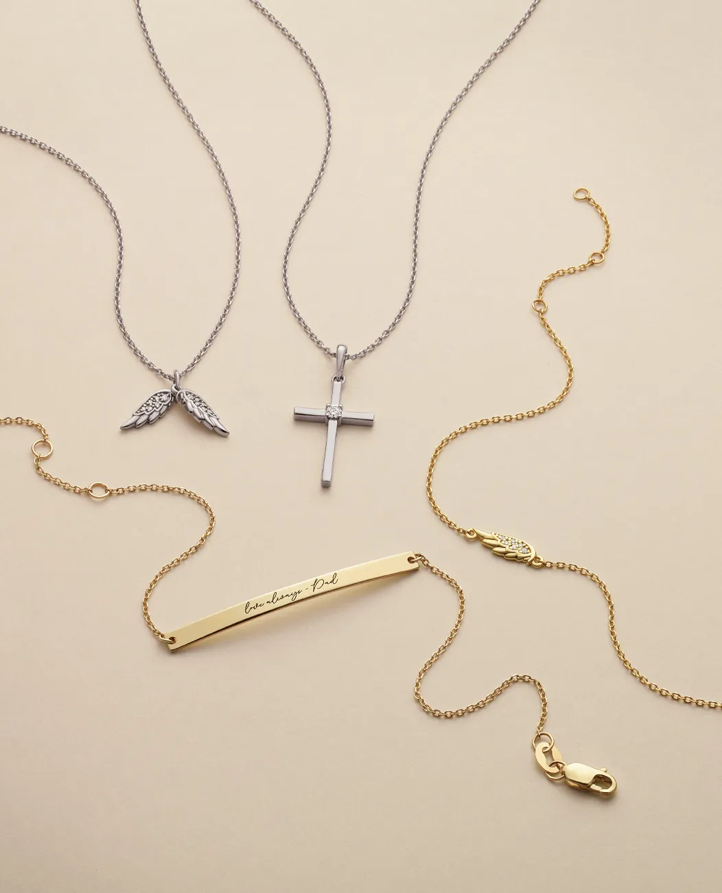 Silver and gold religious necklaces with cross, wings, and engraved bar.