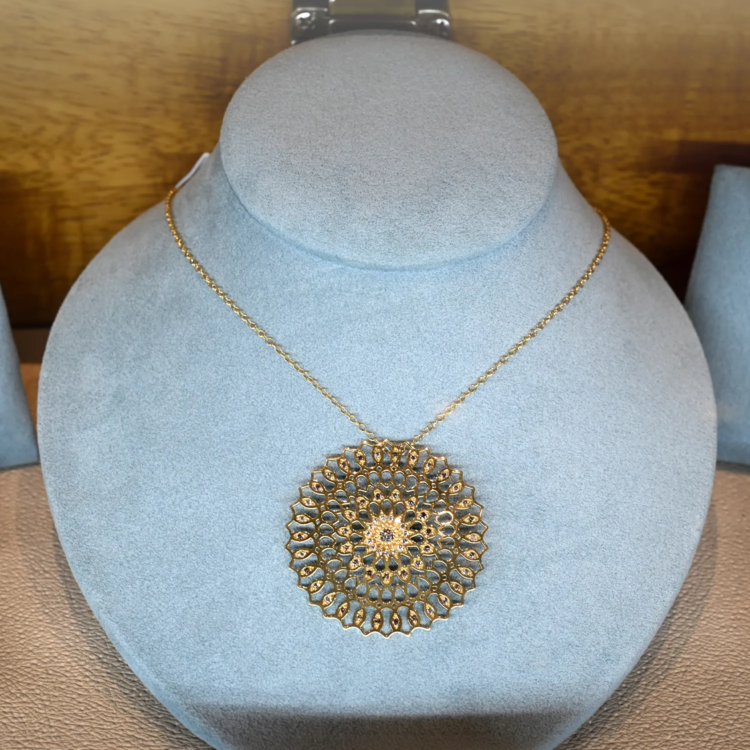 Elegant gold necklace with intricate circular pendant on a display bust.