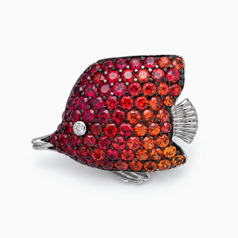 A fish-shaped brooch adorned with red and orange gemstones on a silver base.