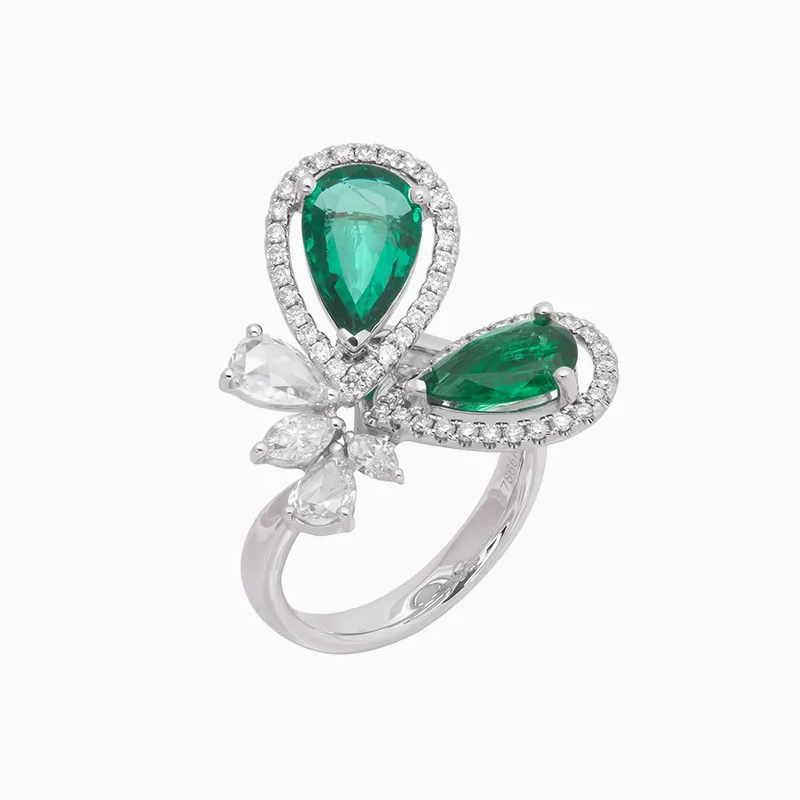 A silver ring with two large green emeralds and small white diamonds in a floral design.