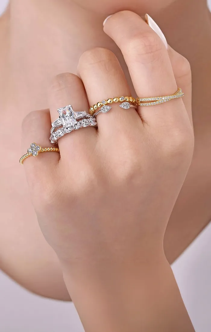 Hand adorned with multiple gold and diamond rings. Shop Gabriel & Co. Bridal.
