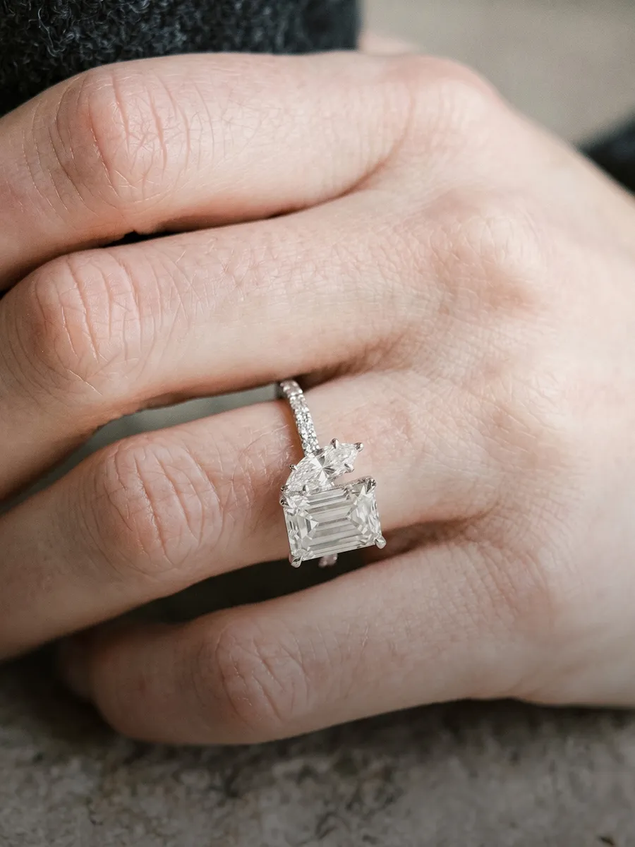 A hand wearing a large, square-cut diamond engagement ring with a detailed band.