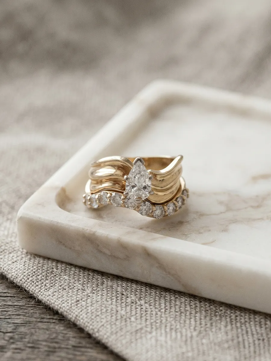 Gold ring with pear-shaped diamond and small diamonds on a marble tray.