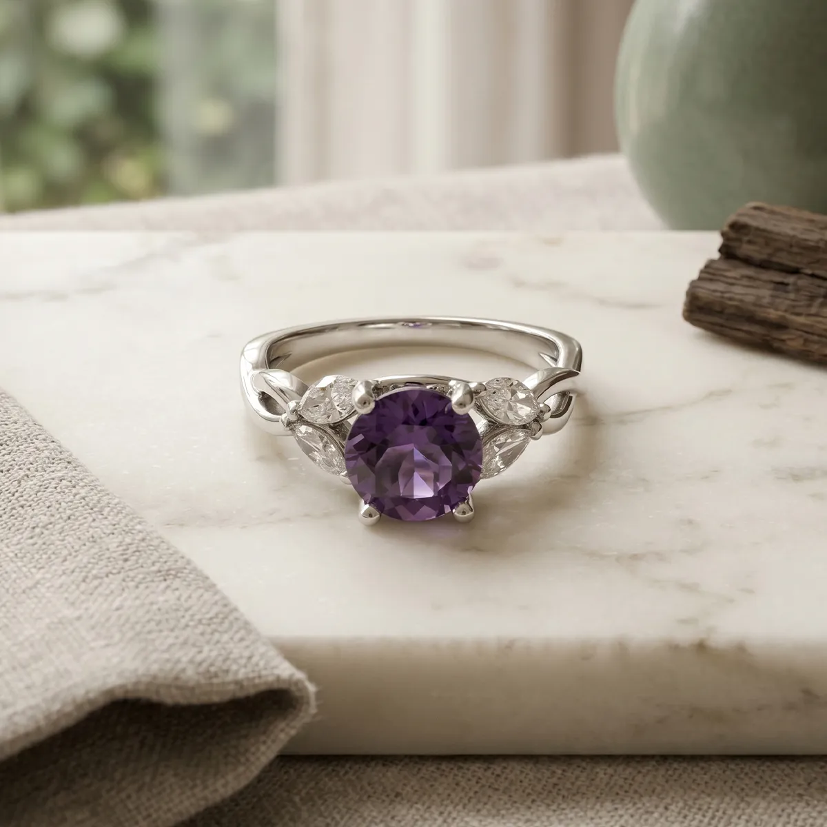 Silver ring with a purple gemstone and diamond accents on a marble surface.