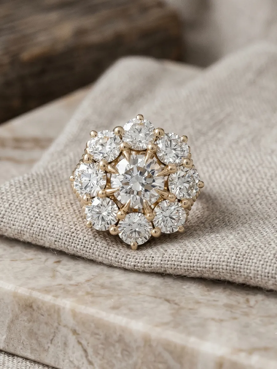 A gold ring with a central diamond surrounded by smaller diamonds on a fabric surface.