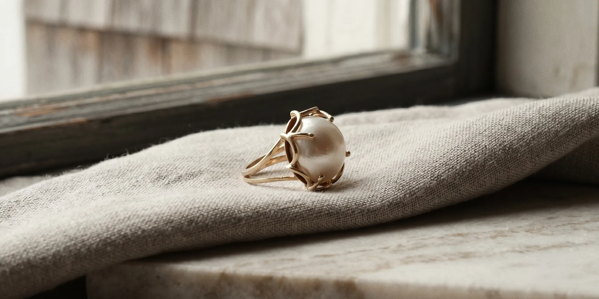 Gold ring with a large pearl on a beige fabric. Learn about heirloom redesign.