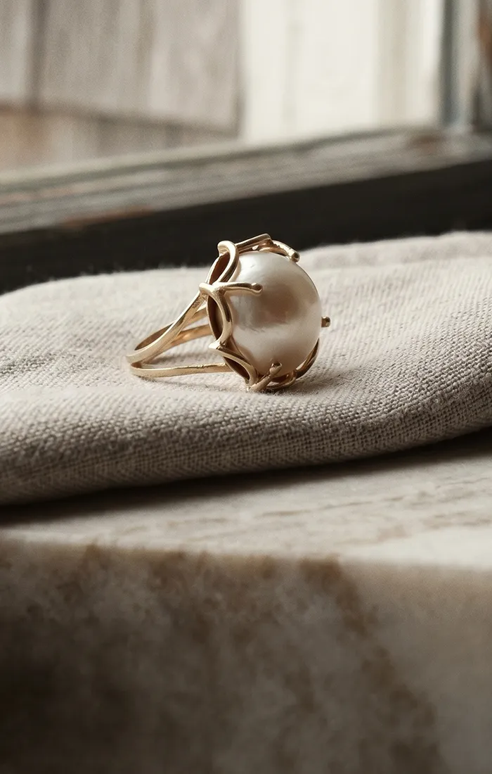 Gold ring with a large pearl on a beige fabric. Learn about heirloom redesign.