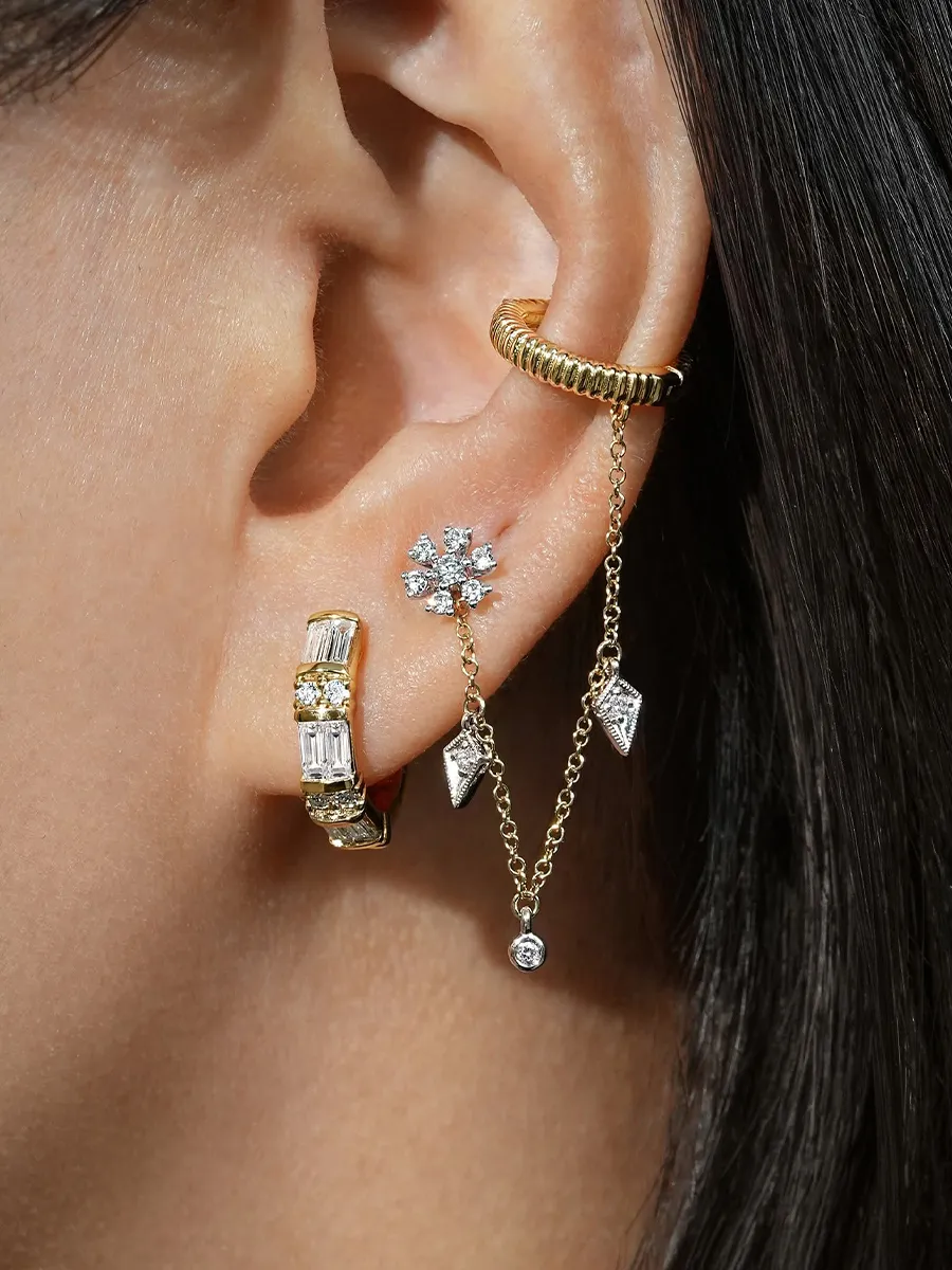 A close-up of an ear adorned with multiple gold and diamond earrings, including a chain and hoop design.
