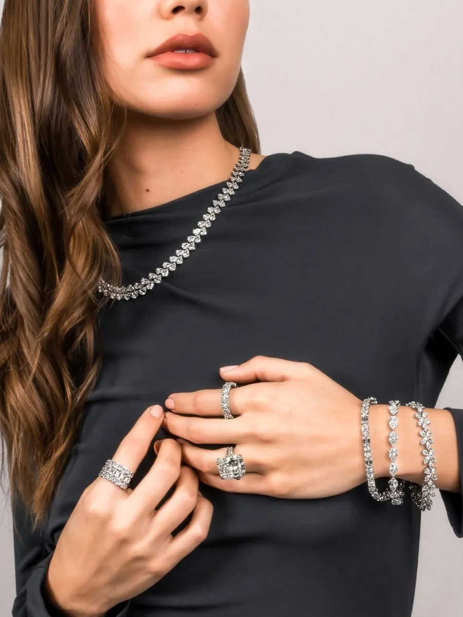 A woman wearing a dark top showcases diamond jewelry, including a necklace, rings, and bracelets.