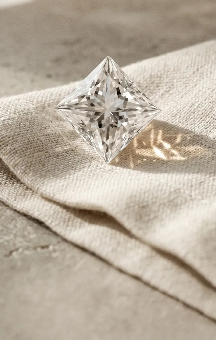 Square-cut diamond on textured fabric, showcasing brilliance. Read our guide on natural vs. lab-grown diamonds.