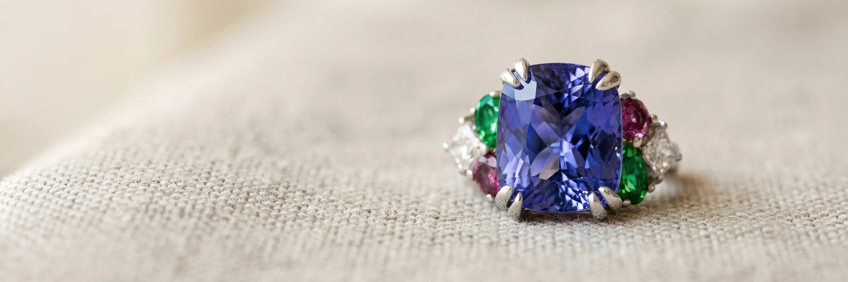 Custom ring with a large blue gemstone, surrounded by green, red, and white stones. Start a Project at Hingham Jewelers.