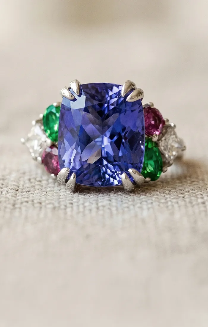 Custom ring with a large blue gemstone, surrounded by green, red, and white stones. Start a Project at Hingham Jewelers.