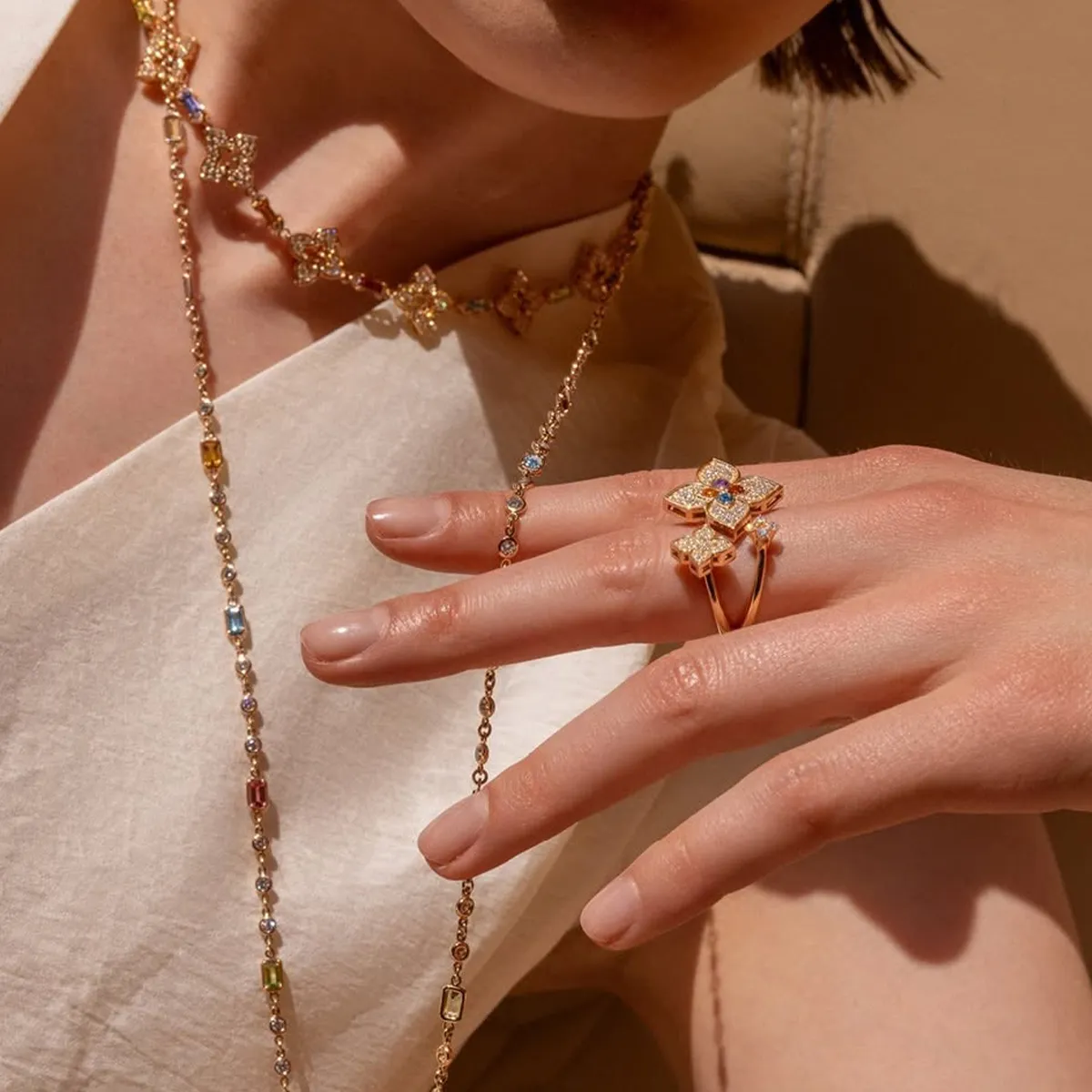 Elegant jewelry set with floral designs on necklace and rings, worn by a person in a light outfit.