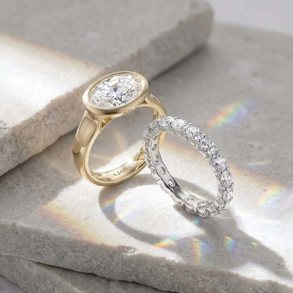 Two elegant rings on stone, one gold with a large diamond, the other silver with smaller diamonds.