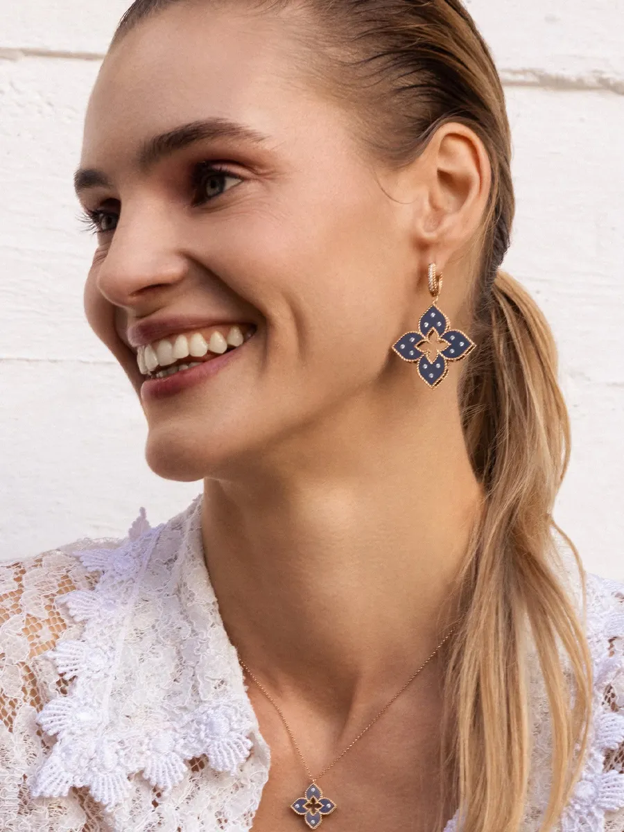 Smiling woman wearing blue floral earrings and necklace, lace top.