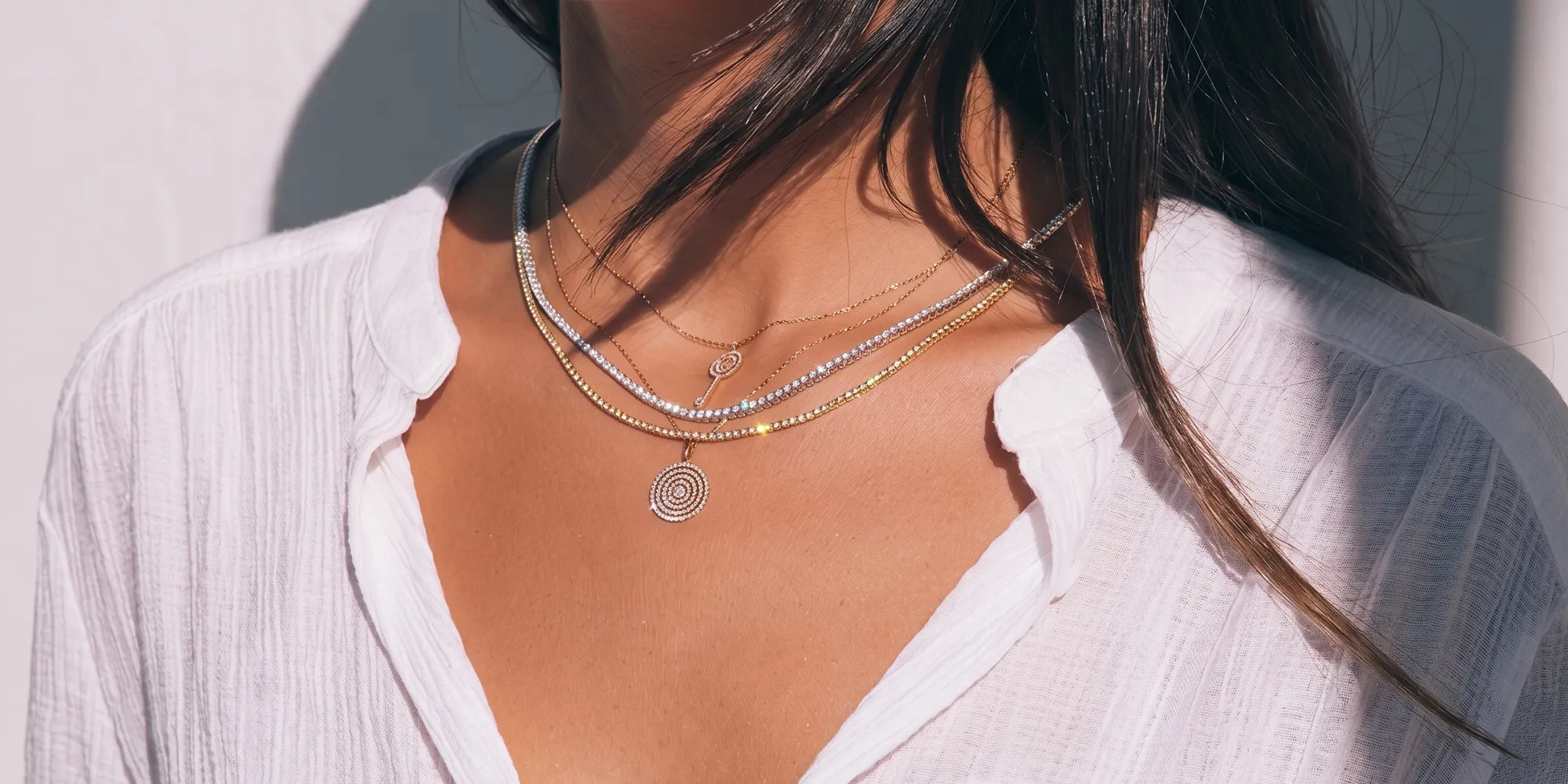 Layered necklaces with circular pendants on a woman wearing a white shirt. Click to shop designer jewelry.