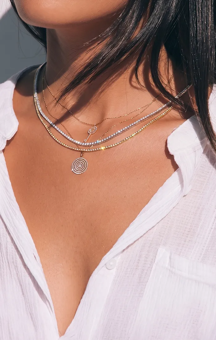 Layered necklaces with circular pendants on a woman wearing a white shirt. Click to shop designer jewelry.