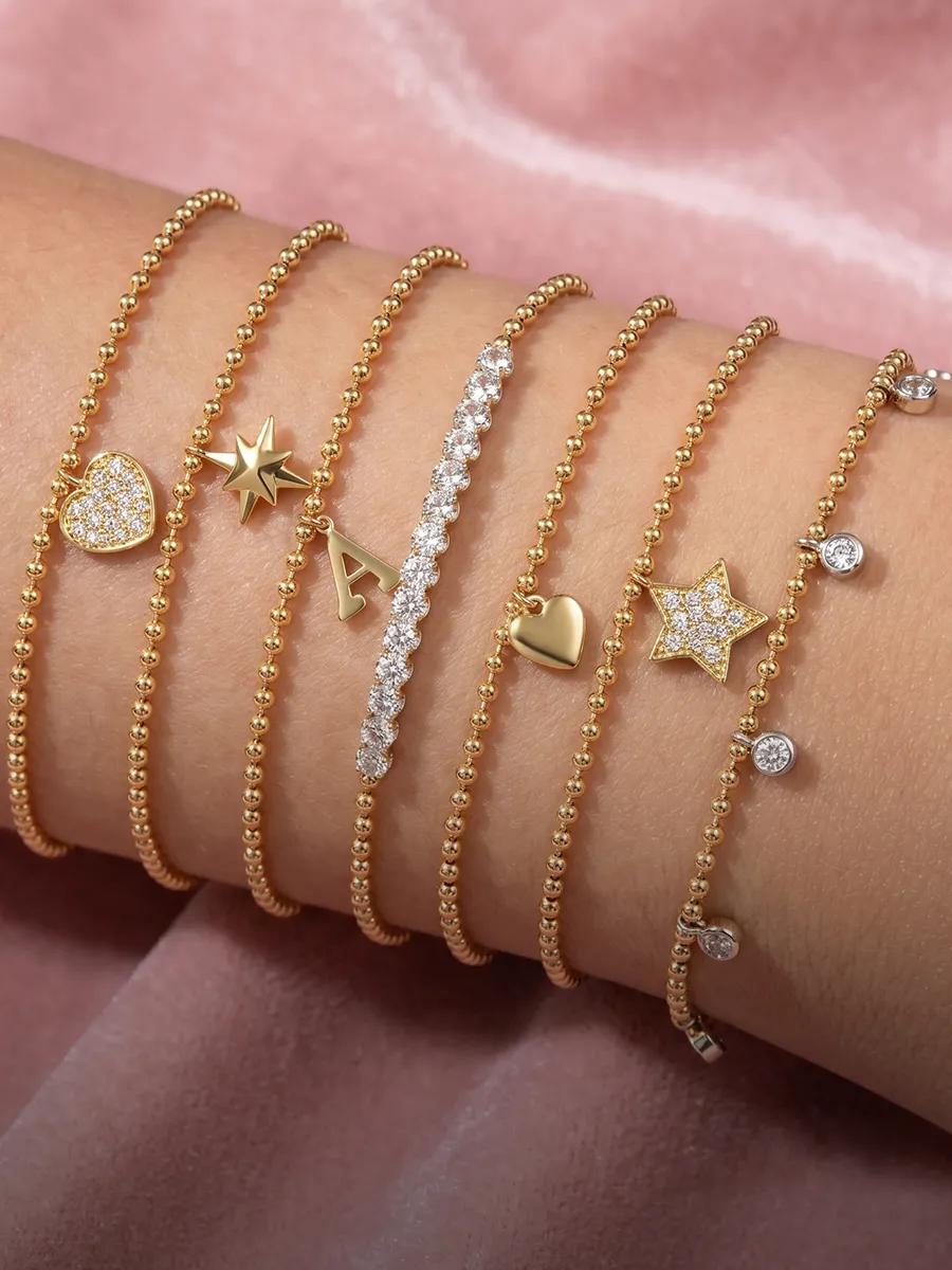 Gold bracelets with charms, including stars, hearts, and an initial, on a wrist. Shop charms at Hingham Jewelers.