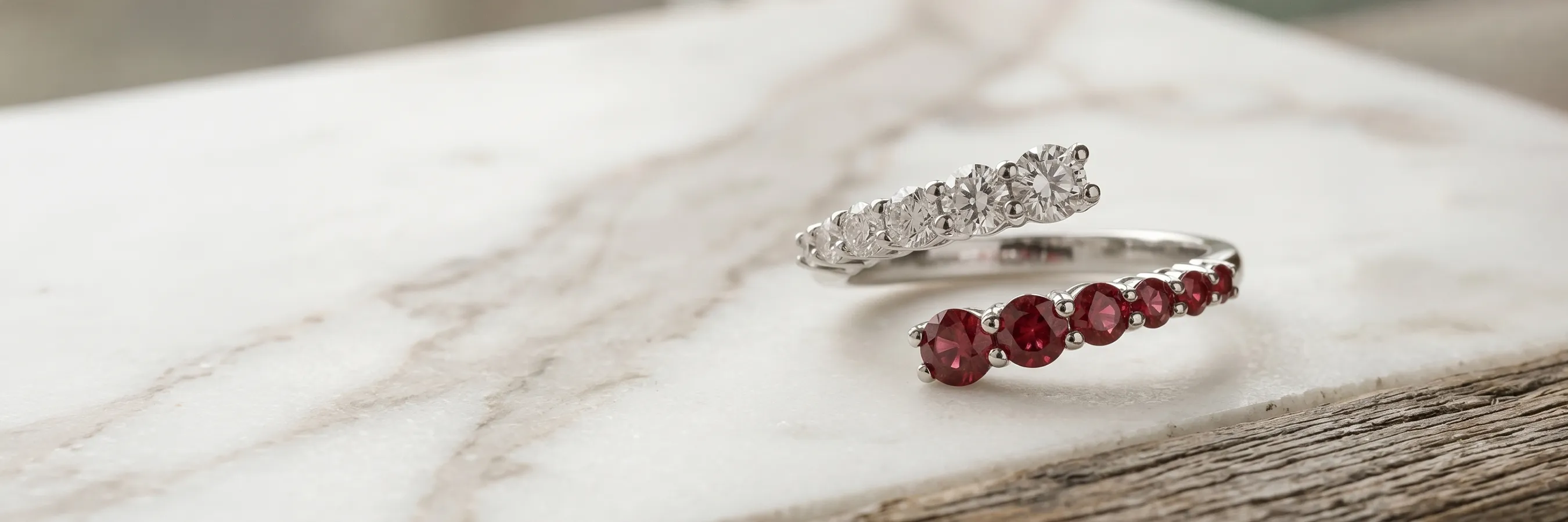 Two silver rings with red and clear gemstones on a wooden surface. Explore H.J. Signature Collection.