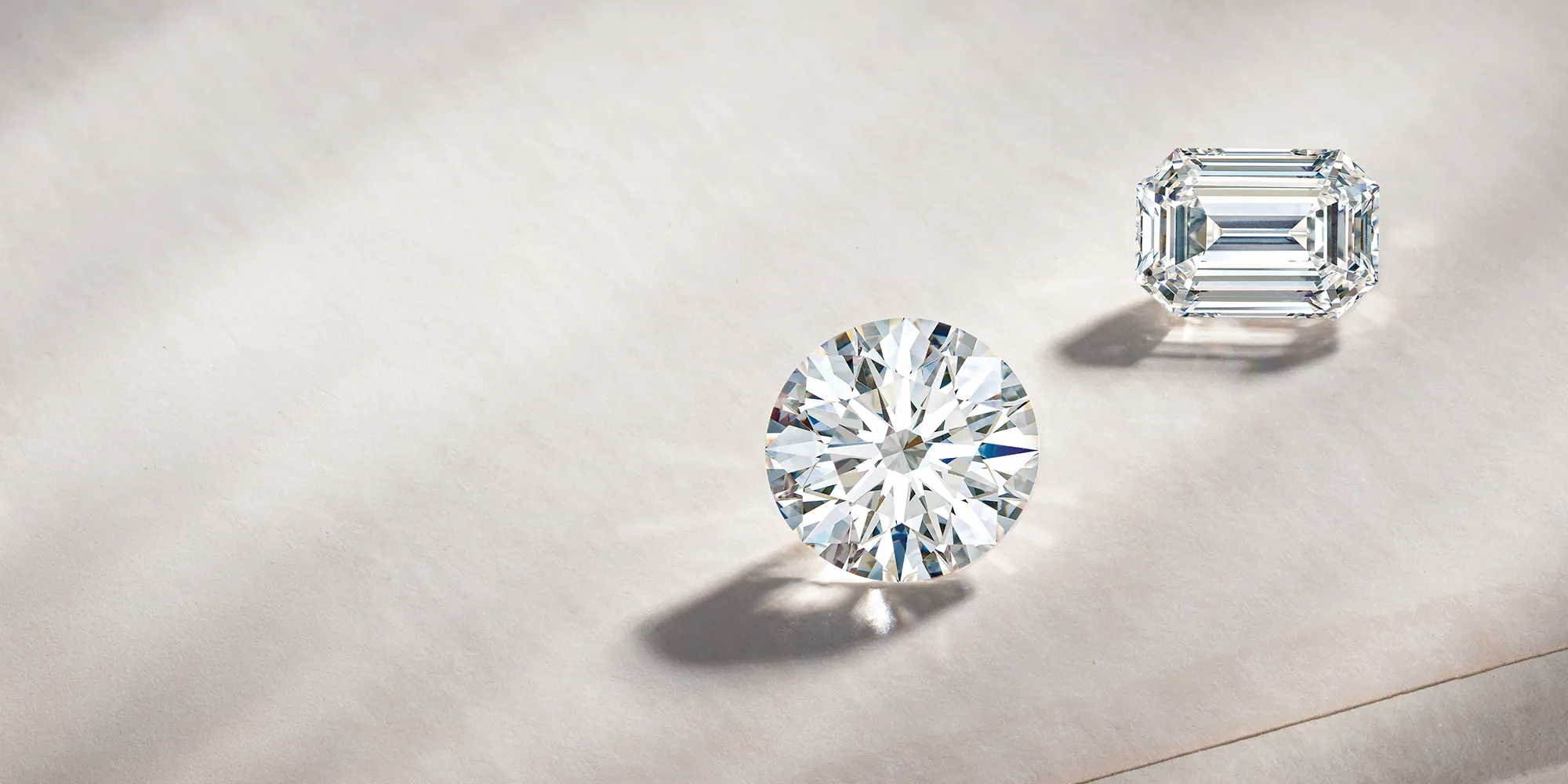 Two loose diamonds, one round and one emerald cut, on a soft surface.