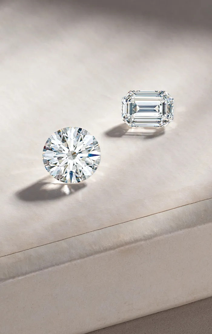 Two loose diamonds, one round and one emerald cut, on a soft surface.