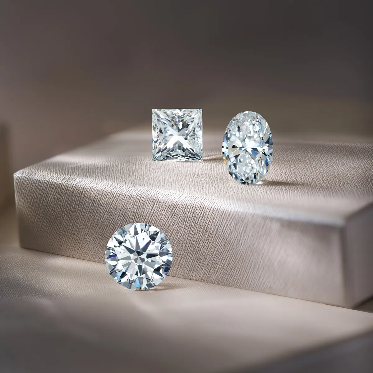 Three sparkling diamonds in different cuts on a textured surface.