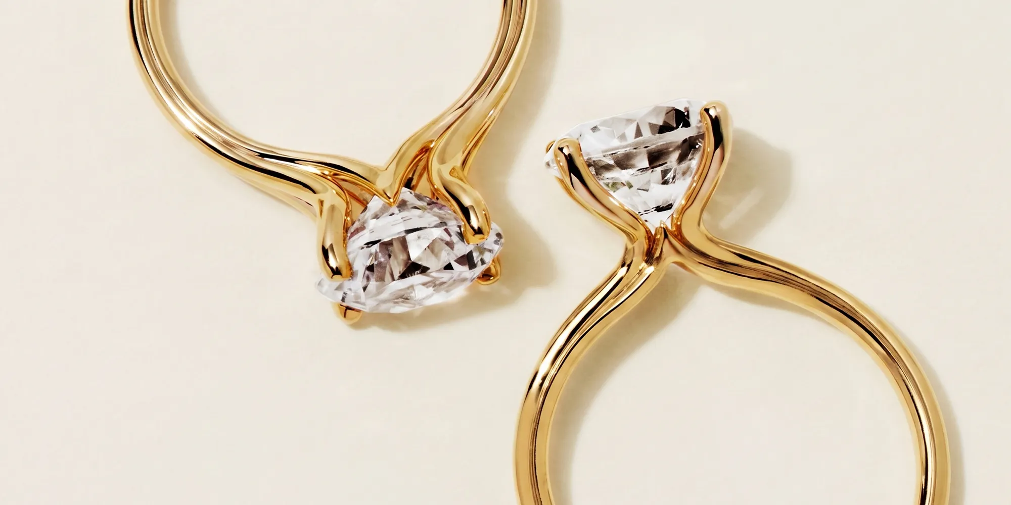 Two gold rings with large, clear gemstones set in elegant prongs on a light background.