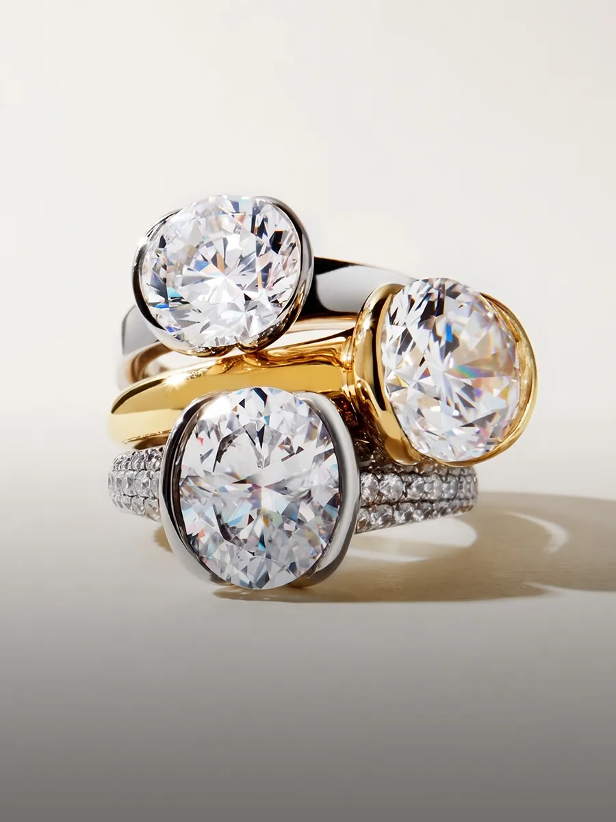 Three elegant rings with large round diamonds in gold and silver settings, stacked together.