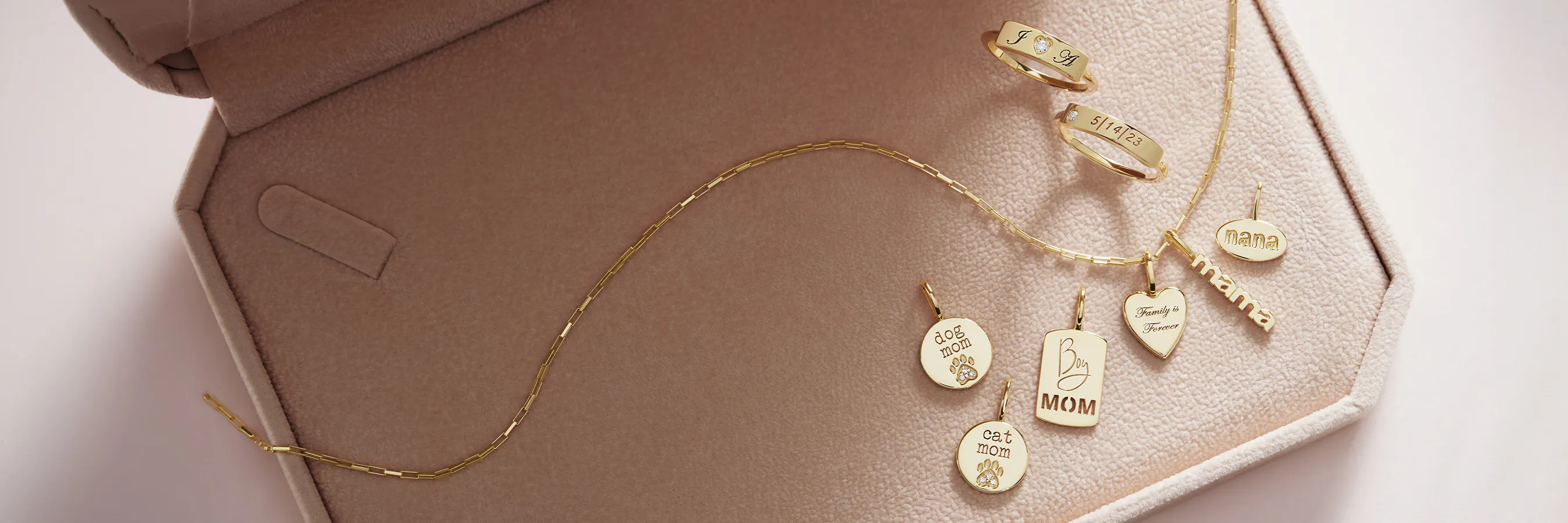 Gold jewelry with engraved pendants and rings on a soft pink surface.