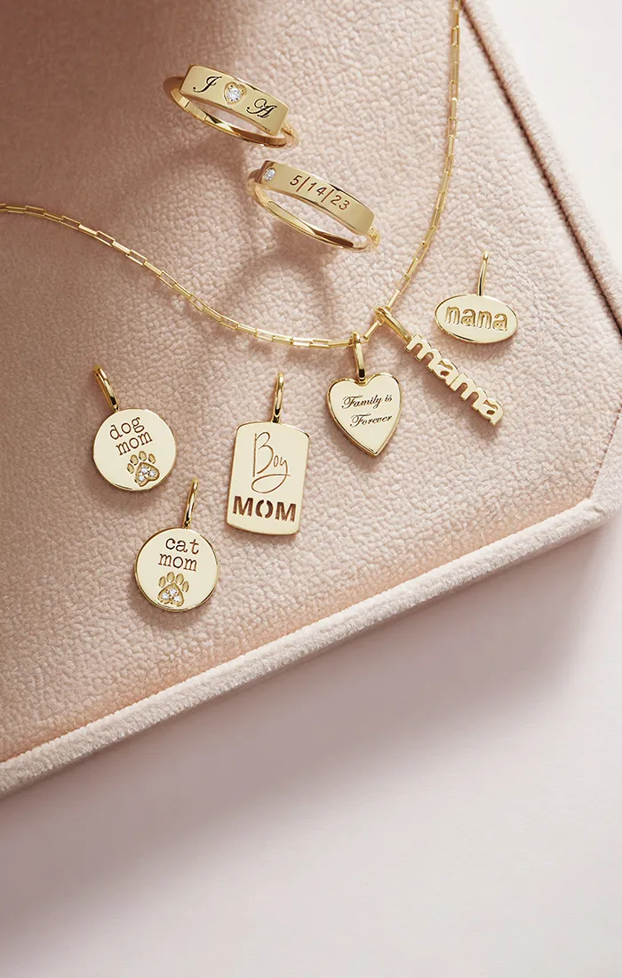 Gold jewelry with engraved pendants and rings on a soft pink surface.
