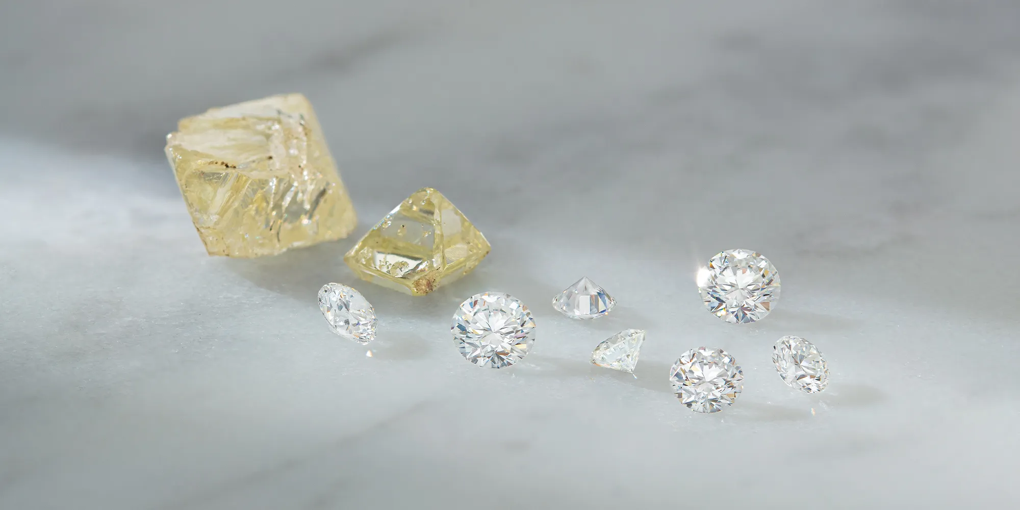 Rough and polished diamonds displayed on a marble surface.