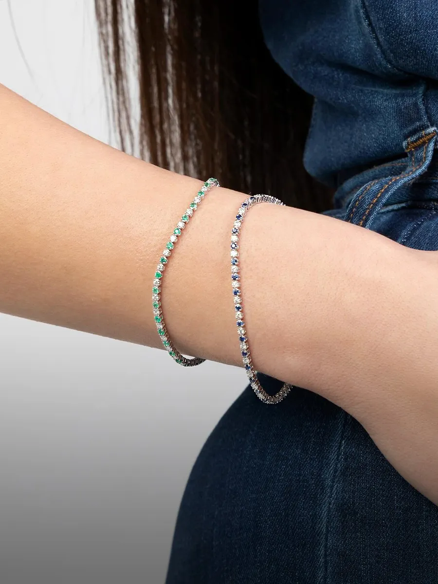 A person wearing two thin, sparkling bracelets on their wrist, with a denim outfit in the background.