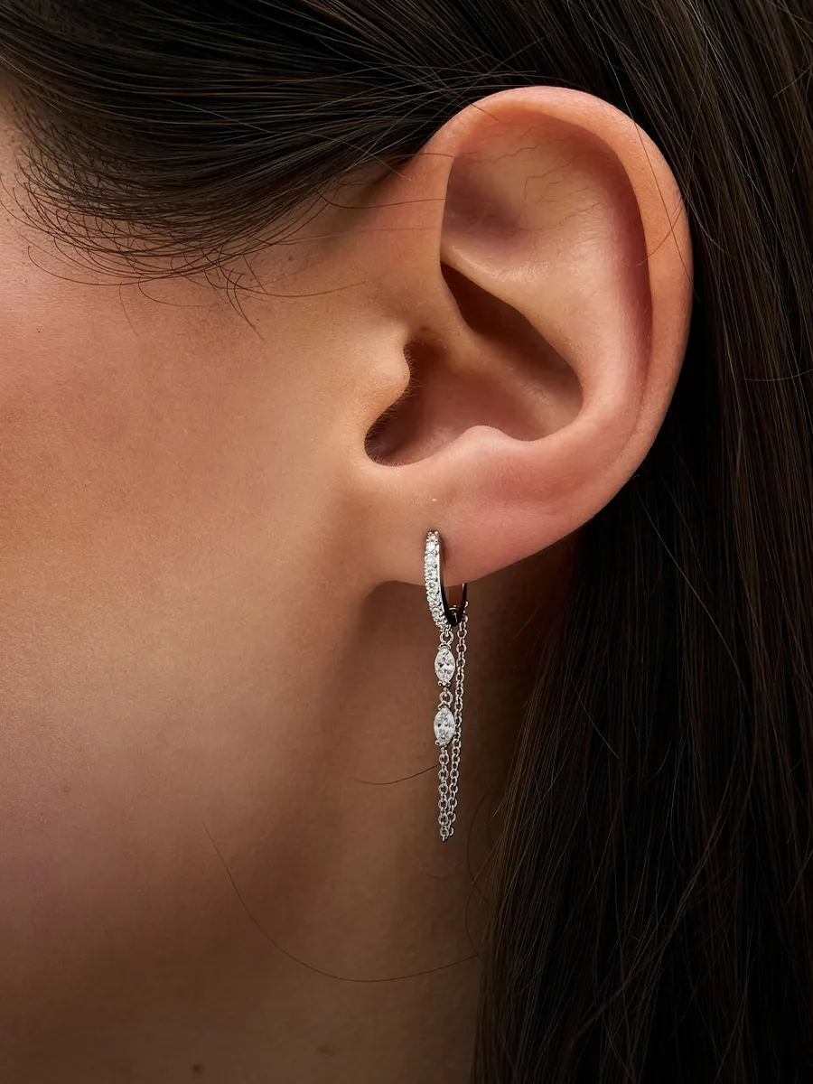 A close-up of an ear wearing a silver earring with dangling chains and gemstones.