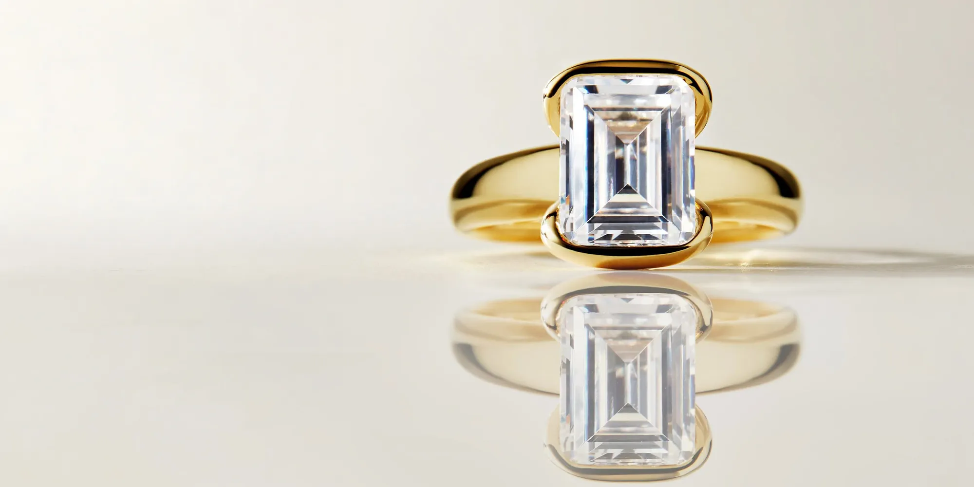 A gold ring with a large, rectangular diamond, reflecting on a smooth surface.